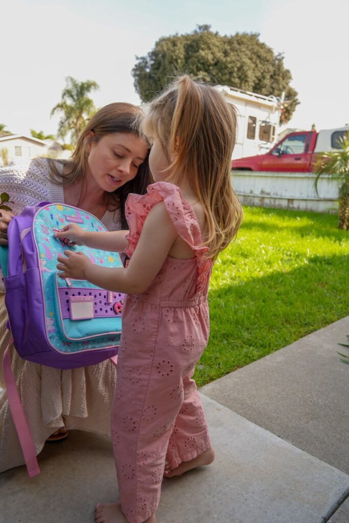 mom helping her daughter zip up her backpack