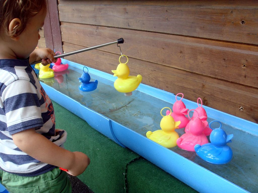 a toddler floating a rubber duck in a water basin