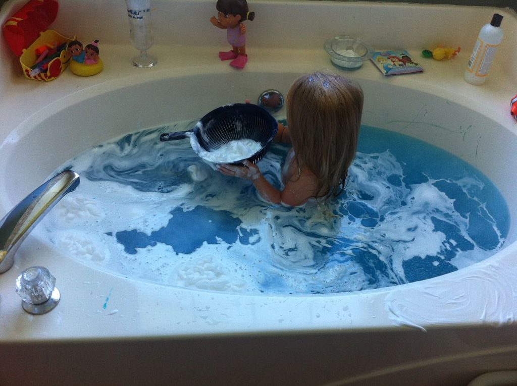 toddler making rain clouds in a tub as water play activities for toddlers