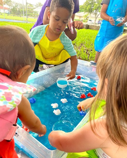 toddler pouring and scooping in a plastic tub as water play activities for toddlers